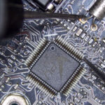 Multimeter probes measuring resistance at a crystal oscillator on a circuit board, indicating potential signal failure during diagnostic testing