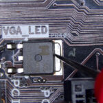 Multimeter measuring a transistor near a VGA LED indicator on a motherboard to locate a short circuit preventing the system from powering on