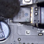 Technician using tweezers and a hot air rework station to remove a Nikos MOSFET from an all-in-one motherboard during repair