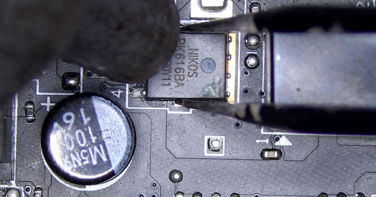 Technician using tweezers and a hot air rework station to remove a Nikos MOSFET from an all-in-one motherboard during repair