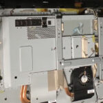 Opened all-in-one computer showing a small 2.5-inch Toshiba hard drive positioned for replacement inside the unit