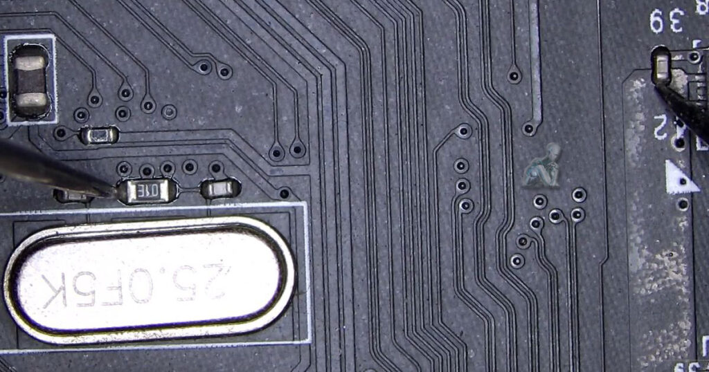 Multimeter probes checking continuity between a capacitor and a resistor near a crystal oscillator on a motherboard during diagnostic work