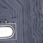 Multimeter probes checking continuity between a capacitor and a resistor near a crystal oscillator on a motherboard during diagnostic work