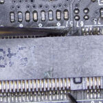 Multimeter probes testing M.2 connector pins on a motherboard to check for short circuits and continuity during diagnostic work