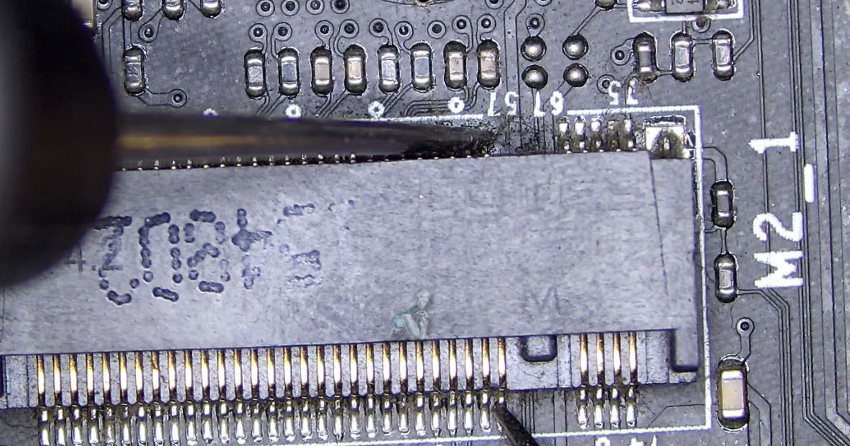 Multimeter probes testing M.2 connector pins on a motherboard to check for short circuits and continuity during diagnostic work