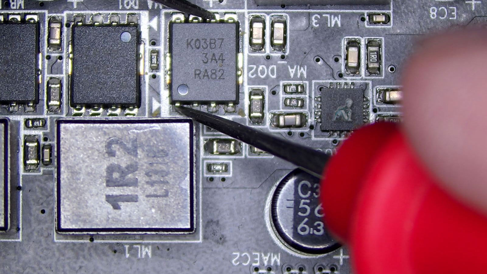 Multimeter probes testing a MOSFET on a gaming console circuit board to analyze electrical behavior during diagnostics