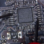 Multimeter probes touching circuit points on a gaming PC motherboard to analyze electrical signals during diagnostic testing