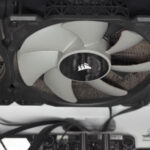 CPU cooling radiator with three attached fans covered in dust and debris being cleaned to restore airflow in a gaming PC system