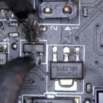 Technician removing a damaged transistor from a desktop motherboard using precision tools during board-level repair