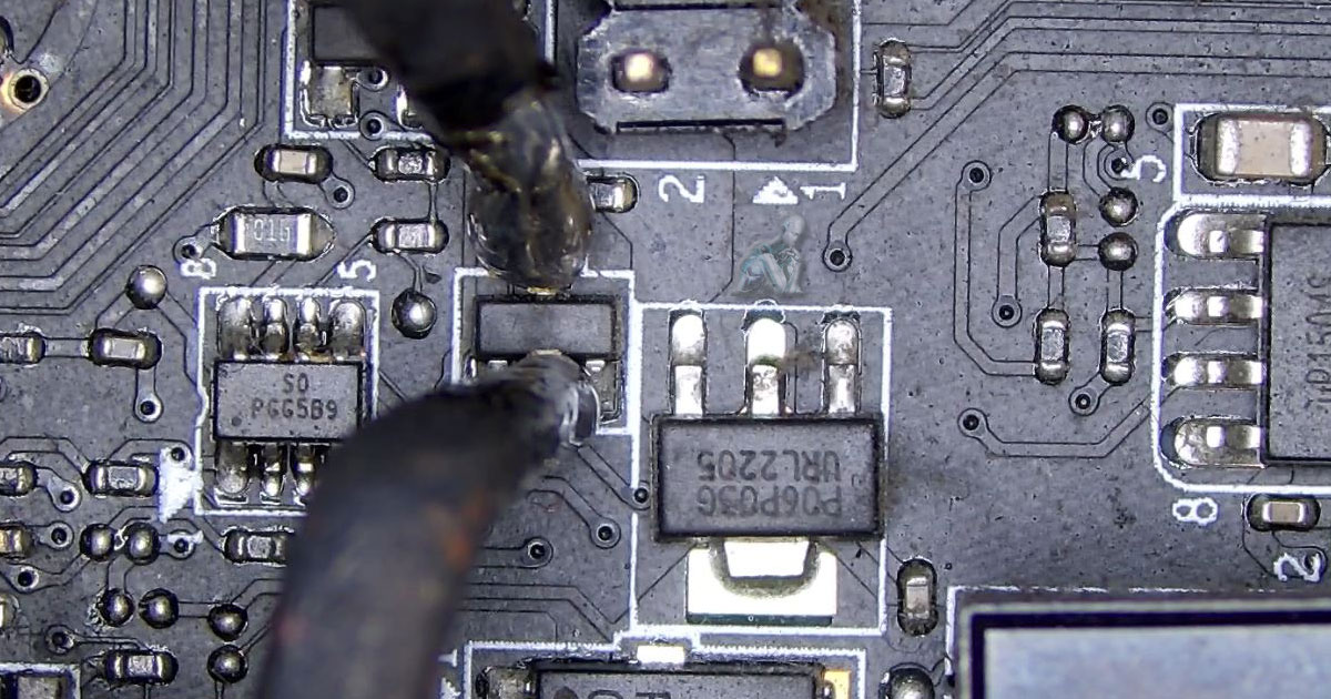 Technician removing a damaged transistor from a desktop motherboard using precision tools during board-level repair
