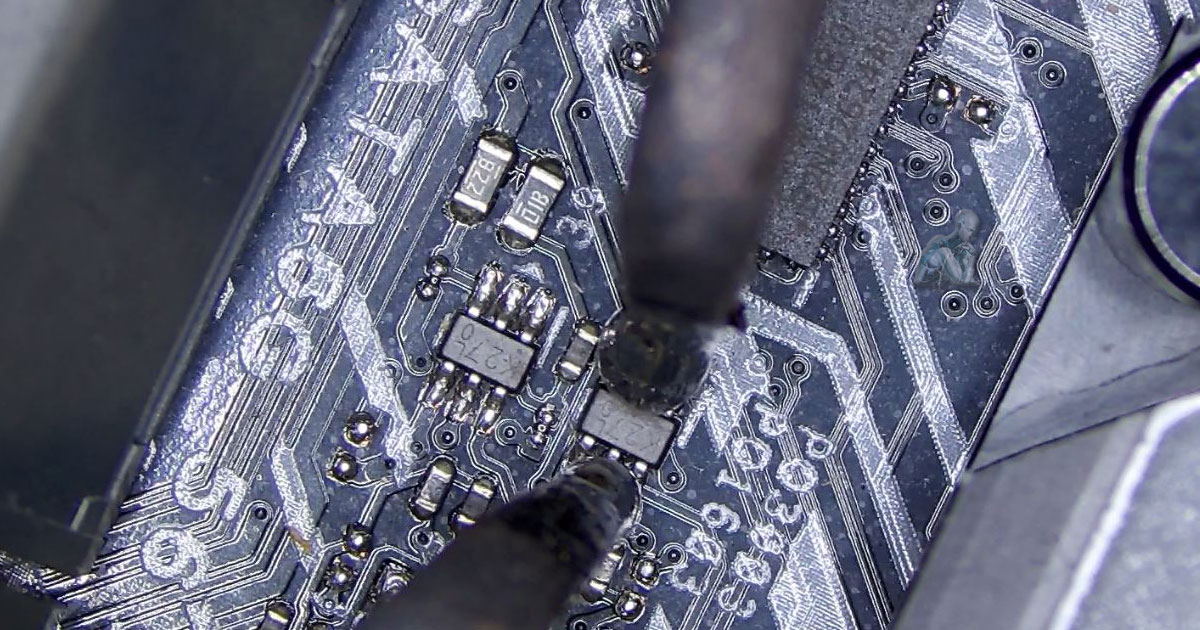 Workbench scene with diagnostic tools arranged for circuit testing, including a multimeter, fine probes, and a motherboard prepared for inspection with visible chips and connectors