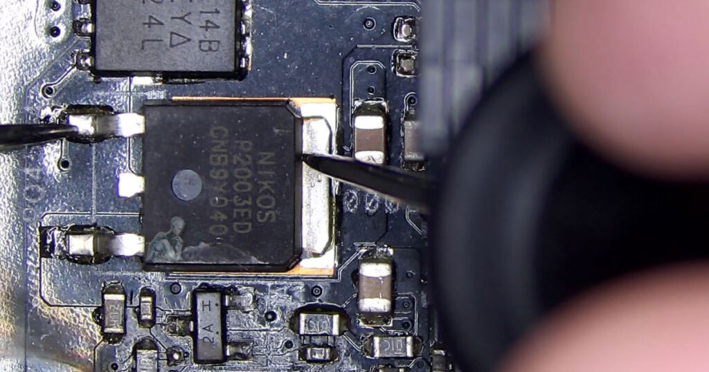 Angled board view showing multimeter probes placed on a NiKo MOSFET to check for a short to ground, with nearby capacitors, resistors, and circuit traces visible