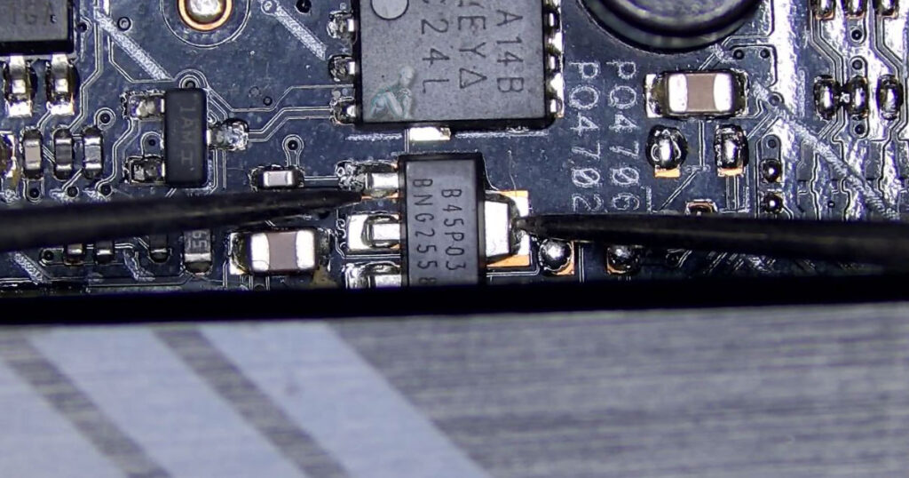 Macro view of a circuit board where multimeter probes are applied to a transistor to check for a short, with nearby resistors and copper traces visible