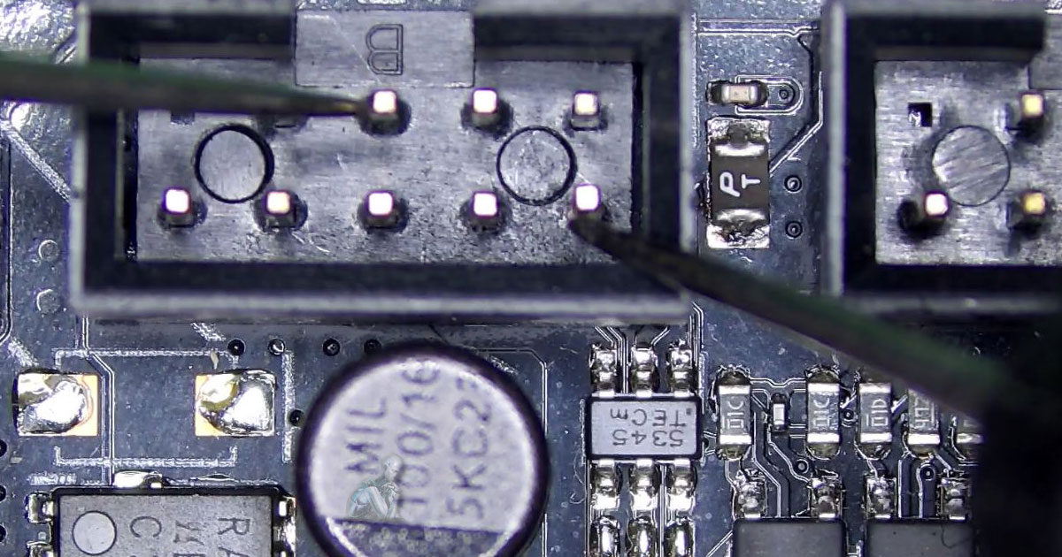 Angled inspection of a circuit board connector while multimeter probes are placed on pins to check for a short, with surrounding ICs and traces visible