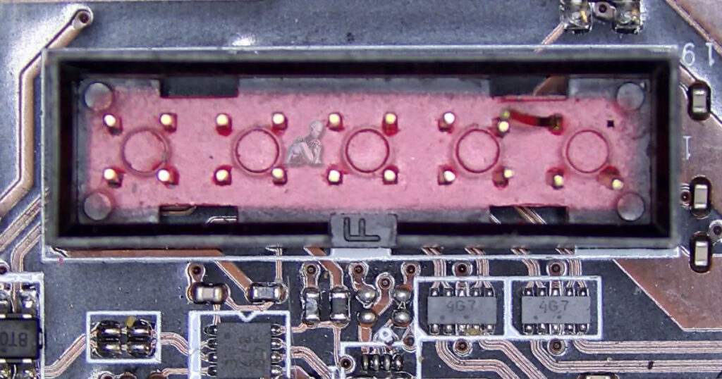 Red plastic multi-pin connector on a circuit board with one corner pin visibly broken and bent downward, indicating physical damage to the component