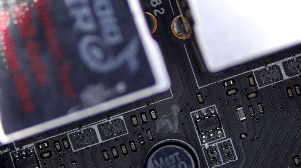 Motherboard area with small components partially hidden behind taller parts, showing a difficult-to-access section being examined during repair work