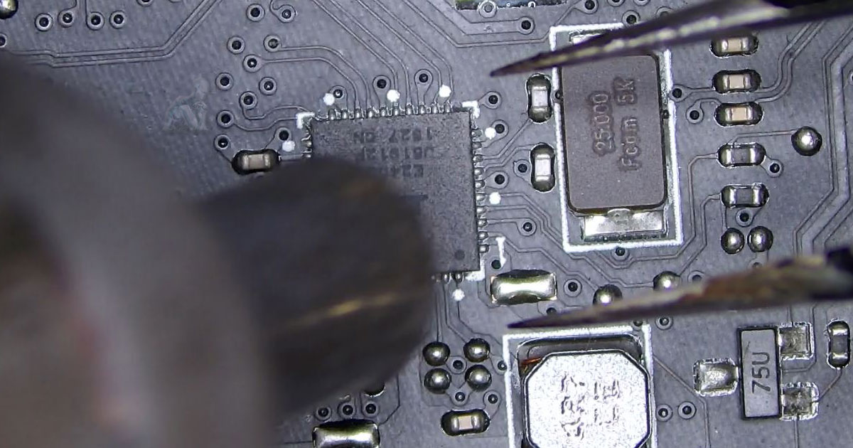 Technician removing a defective electronic component from a circuit board using tools, with surrounding parts exposed during the extraction process