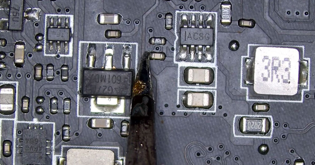Soldering iron tip positioned next to a small SMD capacitor on a circuit board, ready for removal during detailed repair work