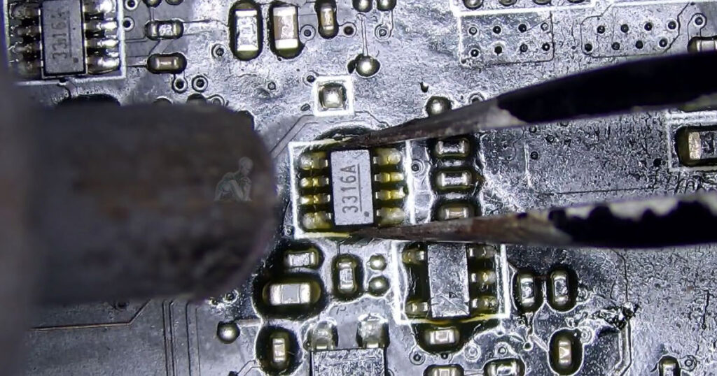 Close-up of a 3316A chip being removed from a motherboard using precision soldering tools with surrounding pads and nearby components visible