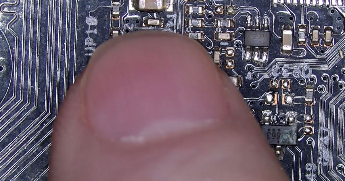 Close-up of a hand gently touching components on a motherboard to detect heat levels, surrounded by chips, capacitors, and integrated circuits during diagnostic testing