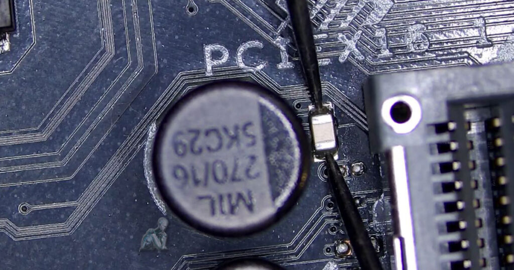 Focused board section where multimeter probes are placed across a small SMD capacitor to test for a short, with nearby ICs and solder joints clearly visible