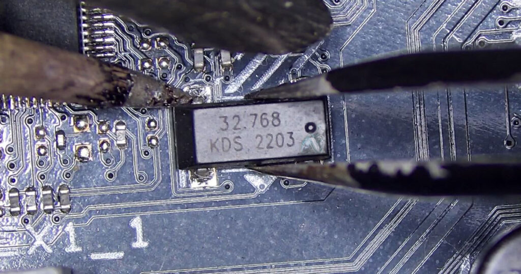 Workbench view of a temperature-controlled soldering station in use on a motherboard, with a fine tip applying heat to components surrounded by pads and traces