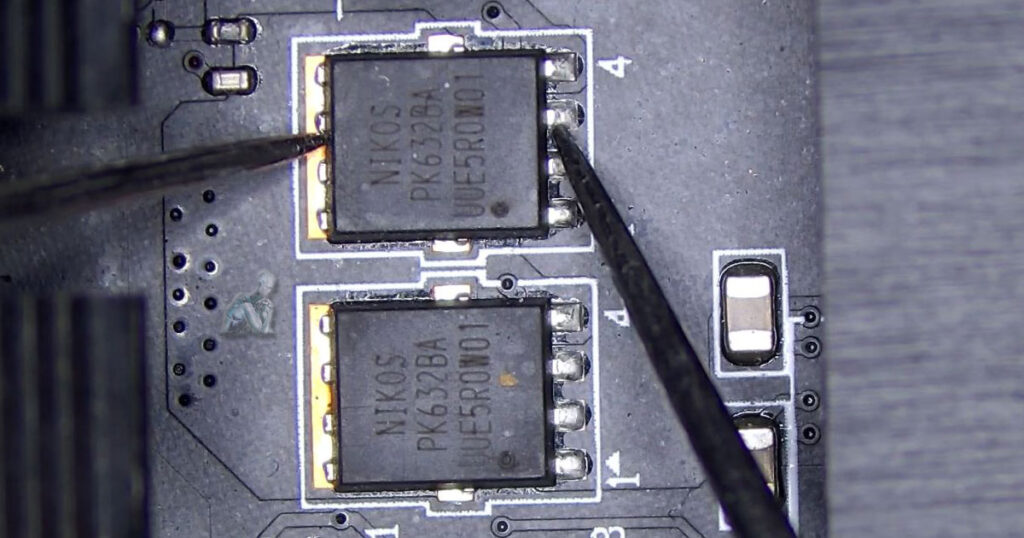 Meter leads placed on a NiKos MOSFET to evaluate low resistance readings, with surrounding capacitors, ICs, and circuit pathways visible
