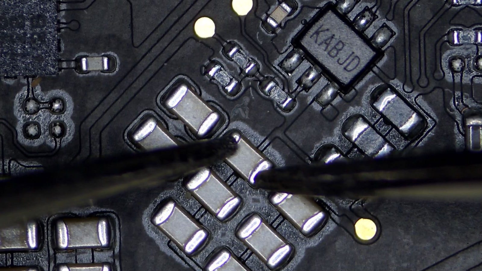 Multimeter probes measuring an SMD capacitor on an iMac circuit board during diagnostic testing