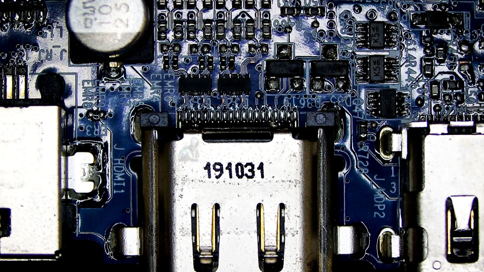 Close-up of a computer circuit board with HDMI connectors, USB port, LAN port, controller chips, capacitors, and small electronic components